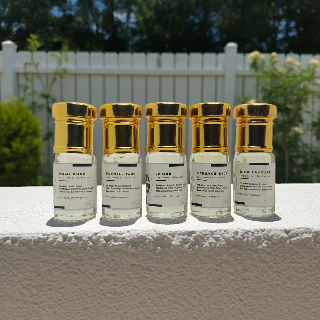 Five small Attar combo bottles with gold caps on a white surface outdoors.
