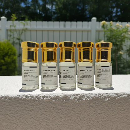 Five small Attar combo bottles with gold caps on a white surface outdoors.